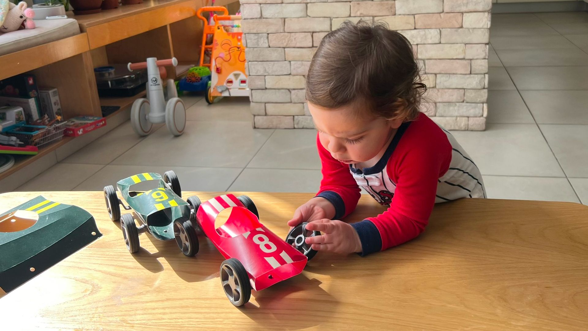 A toddler playing on the floor with red and dark-coloured Bendit cars.