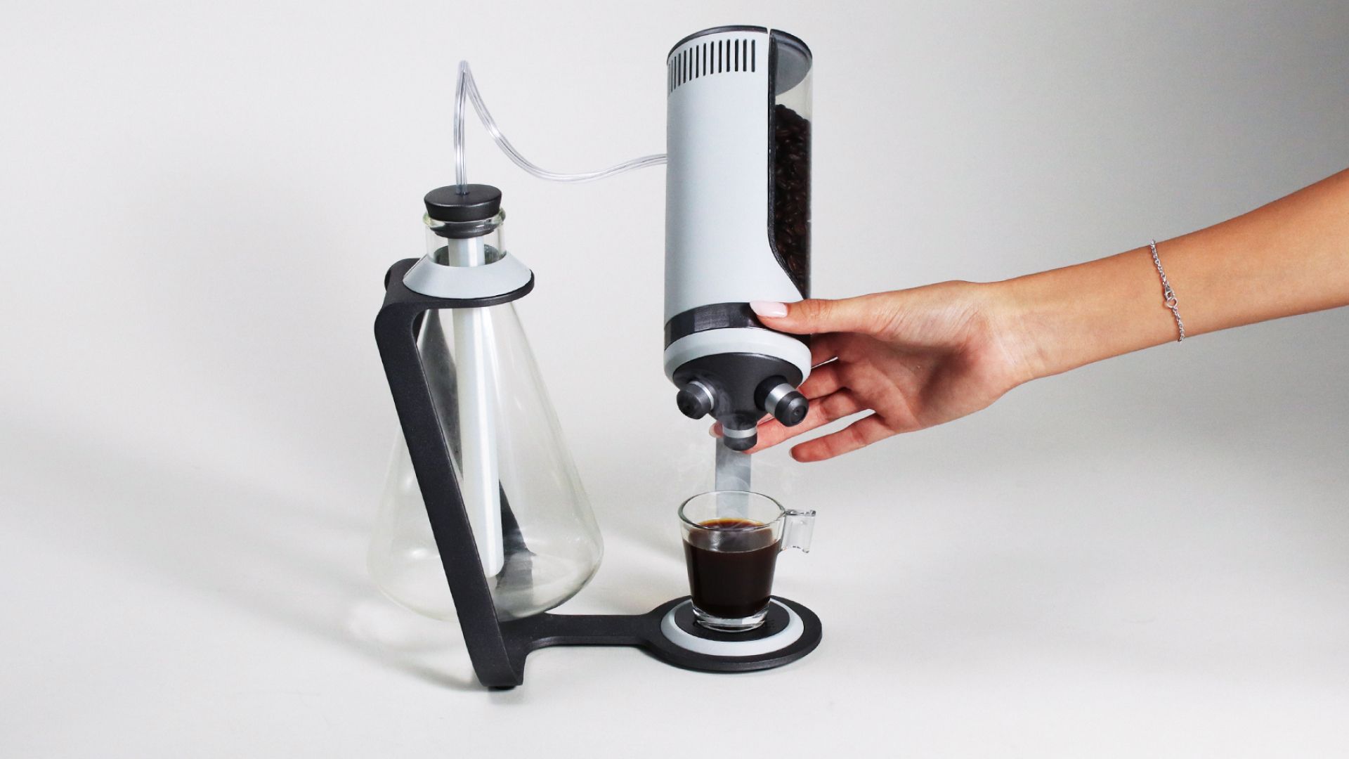 A hand touching the Microcoffee brewer as it dispenses coffee into a small glass.