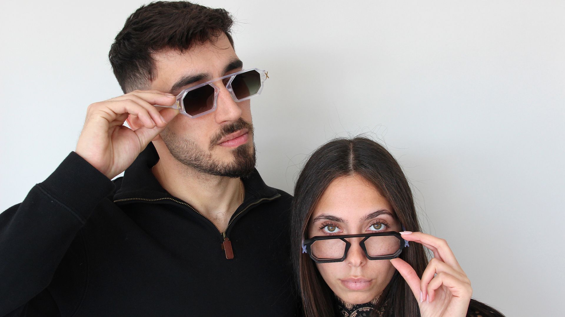 A man and a woman adjusting their Unfoldable eyewear — tinted sunglasses and clear frames.